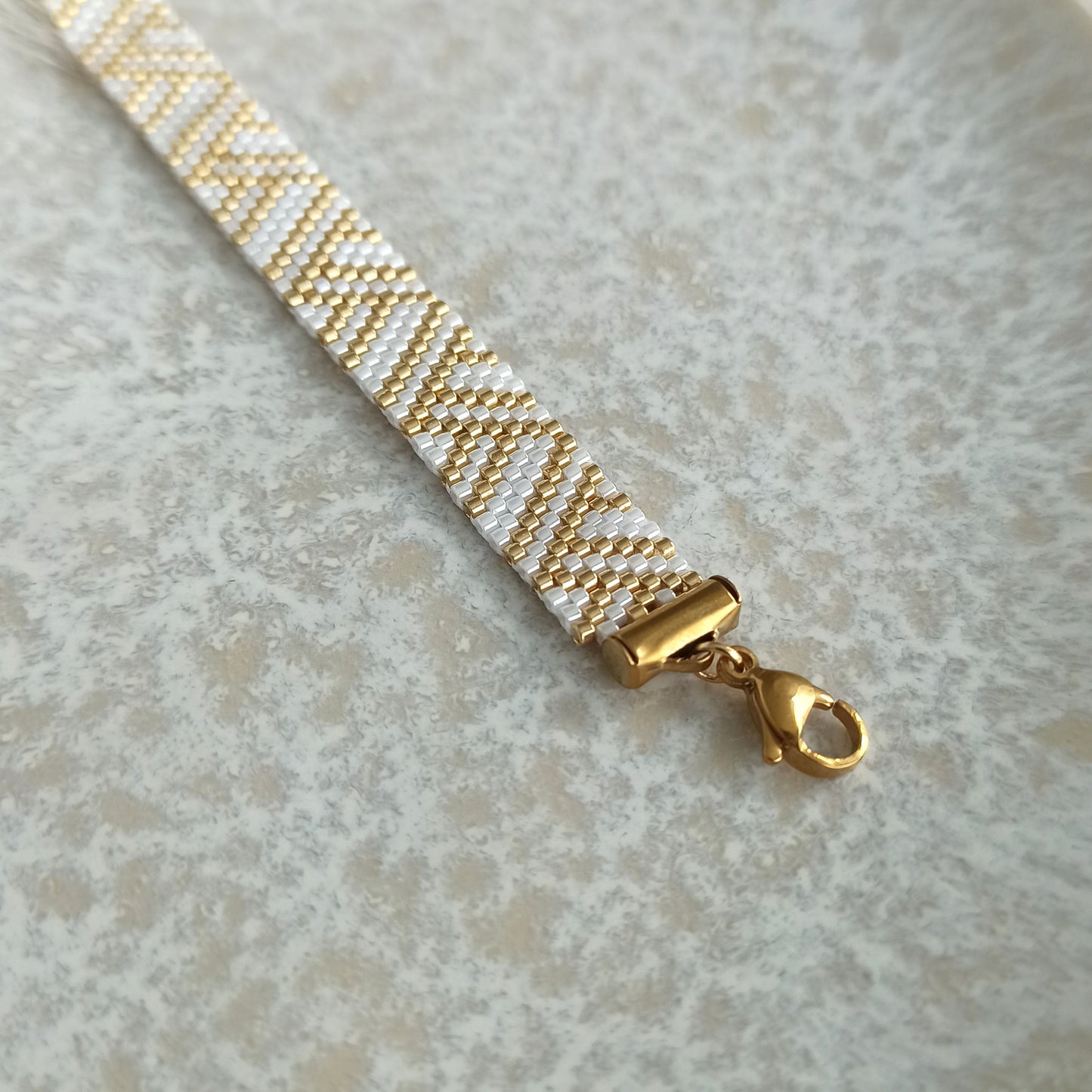 White and Gold Beaded Bracelet with Geometric Pattern

An elegant handmade bracelet featuring a delicate geometric pattern in white and gold tones, creating a timeless and refined look.

The bracelet is made from high-quality Japanese seed beads, known for their precision, subtle shine, and durability. The detailed pattern makes this piece eye-catching yet still elegant.

The clasp is made of gold-plated stainless steel, suitable even for sensitive skin.