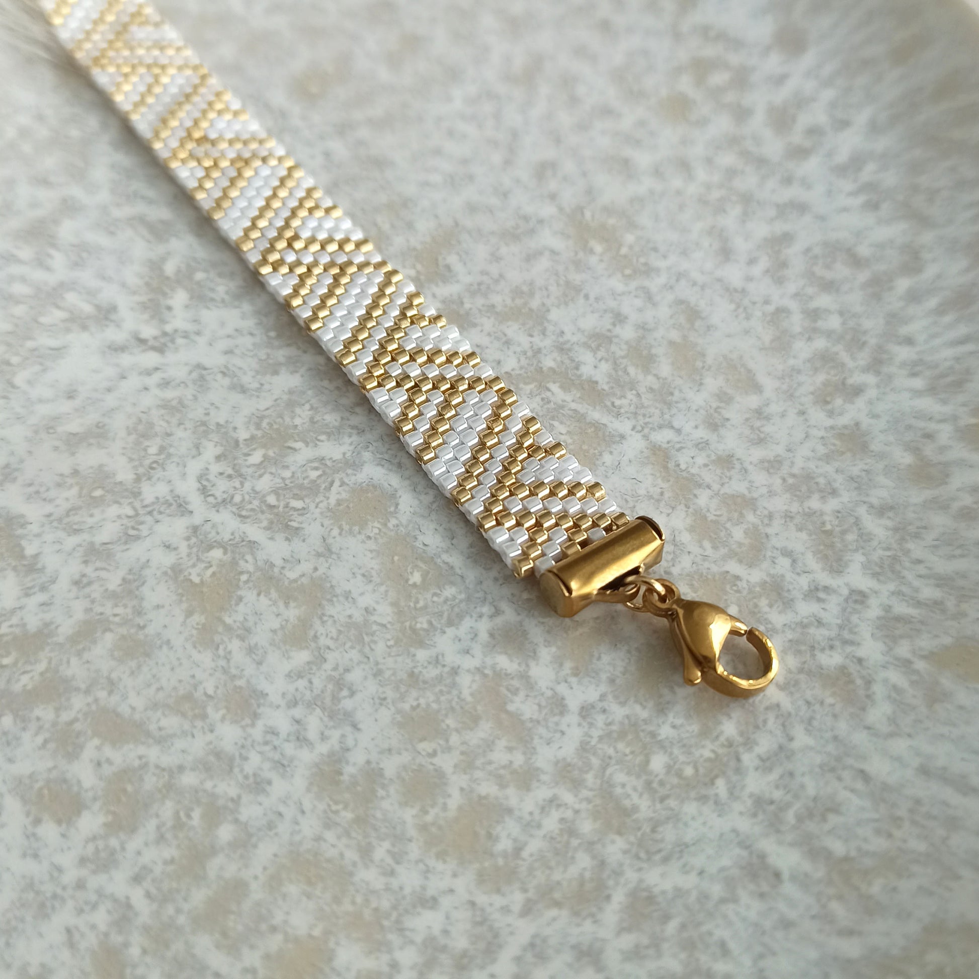 White and Gold Beaded Bracelet with Geometric Pattern

An elegant handmade bracelet featuring a delicate geometric pattern in white and gold tones, creating a timeless and refined look.

The bracelet is made from high-quality Japanese seed beads, known for their precision, subtle shine, and durability. The detailed pattern makes this piece eye-catching yet still elegant.

The clasp is made of gold-plated stainless steel, suitable even for sensitive skin.